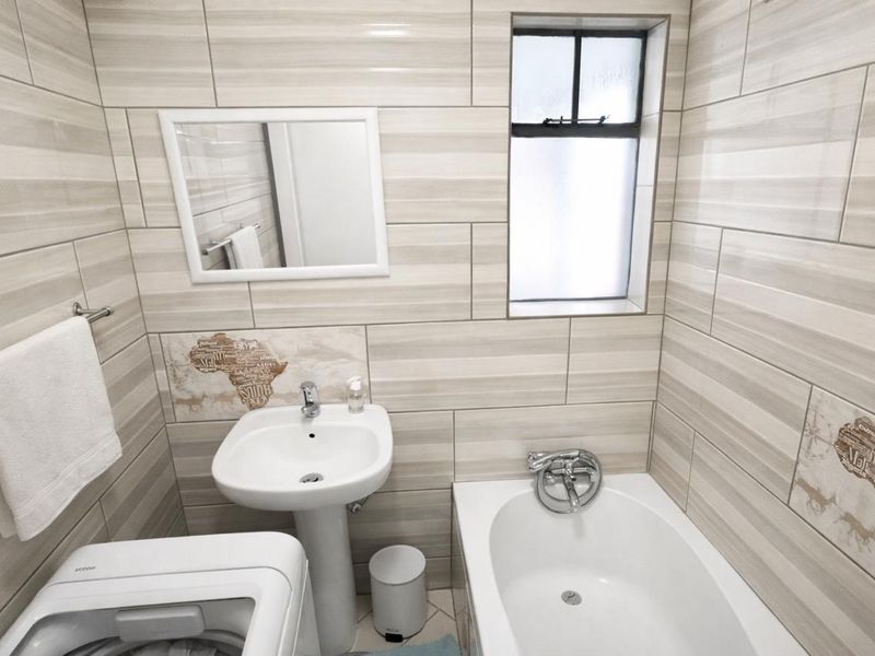 A compact bathroom featuring a pedestal basin, bathtub, and neutral wall tiling with decorative accents.