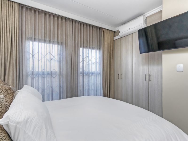A well-maintained bedroom featuring built-in cupboards, a wall-mounted air conditioning unit, and security gates on the windows.