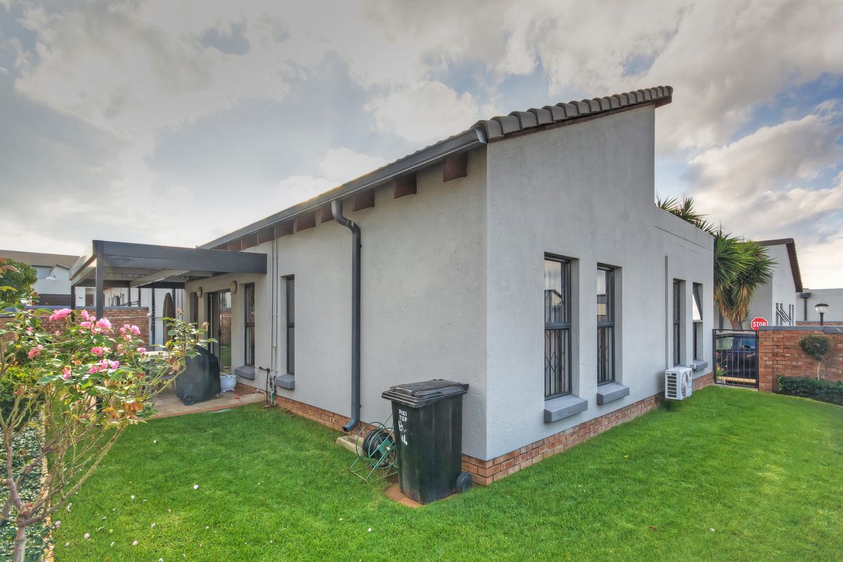 Rear view of the townhouse featuring a covered patio, well-maintained lawn, and exterior wall finishes with security bars on windows.