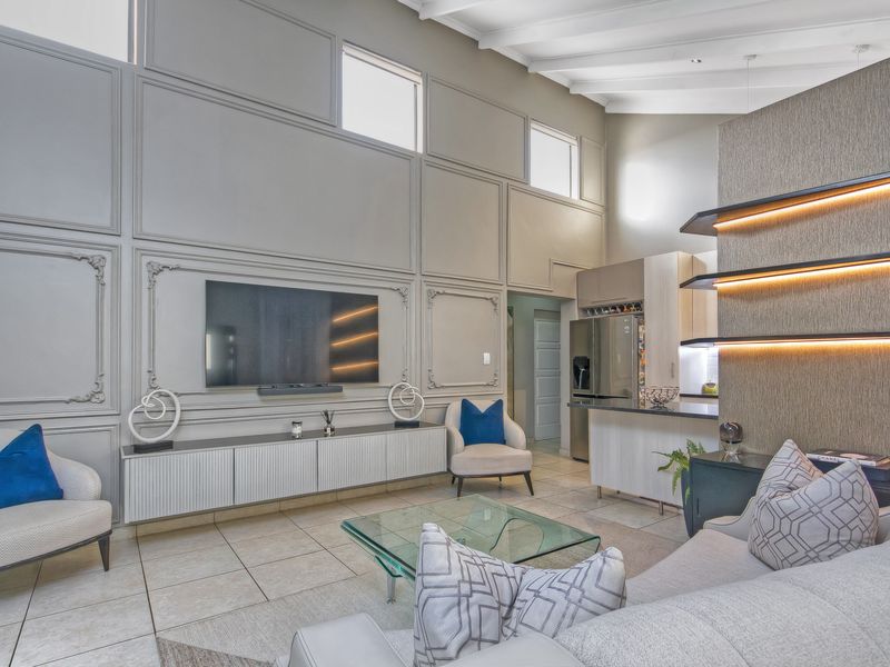 Spacious open-plan living area featuring high vaulted ceilings, elegant wainscoting, modern built-in cabinetry, and integrated LED shelving, seamlessly connecting to a contemporary kitchen.
