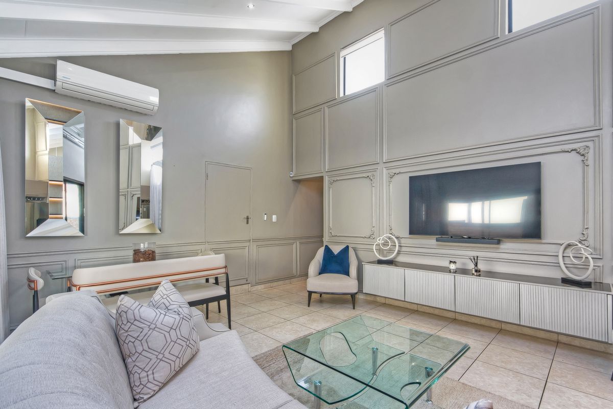 Spacious living room featuring high vaulted ceilings, elegant wall paneling, tiled flooring, and a split-system air conditioner for climate control.