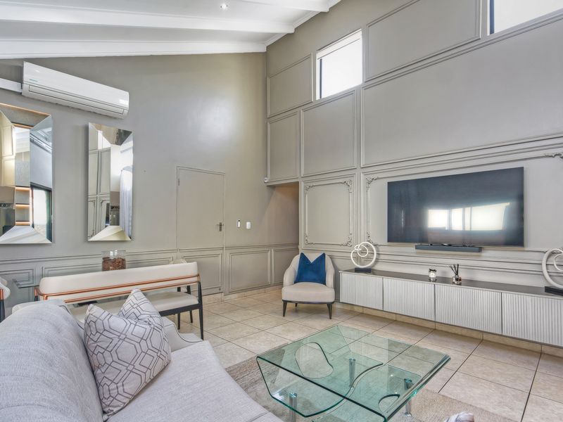 Spacious living room featuring high vaulted ceilings, elegant wall paneling, tiled flooring, and a split-system air conditioner for climate control.