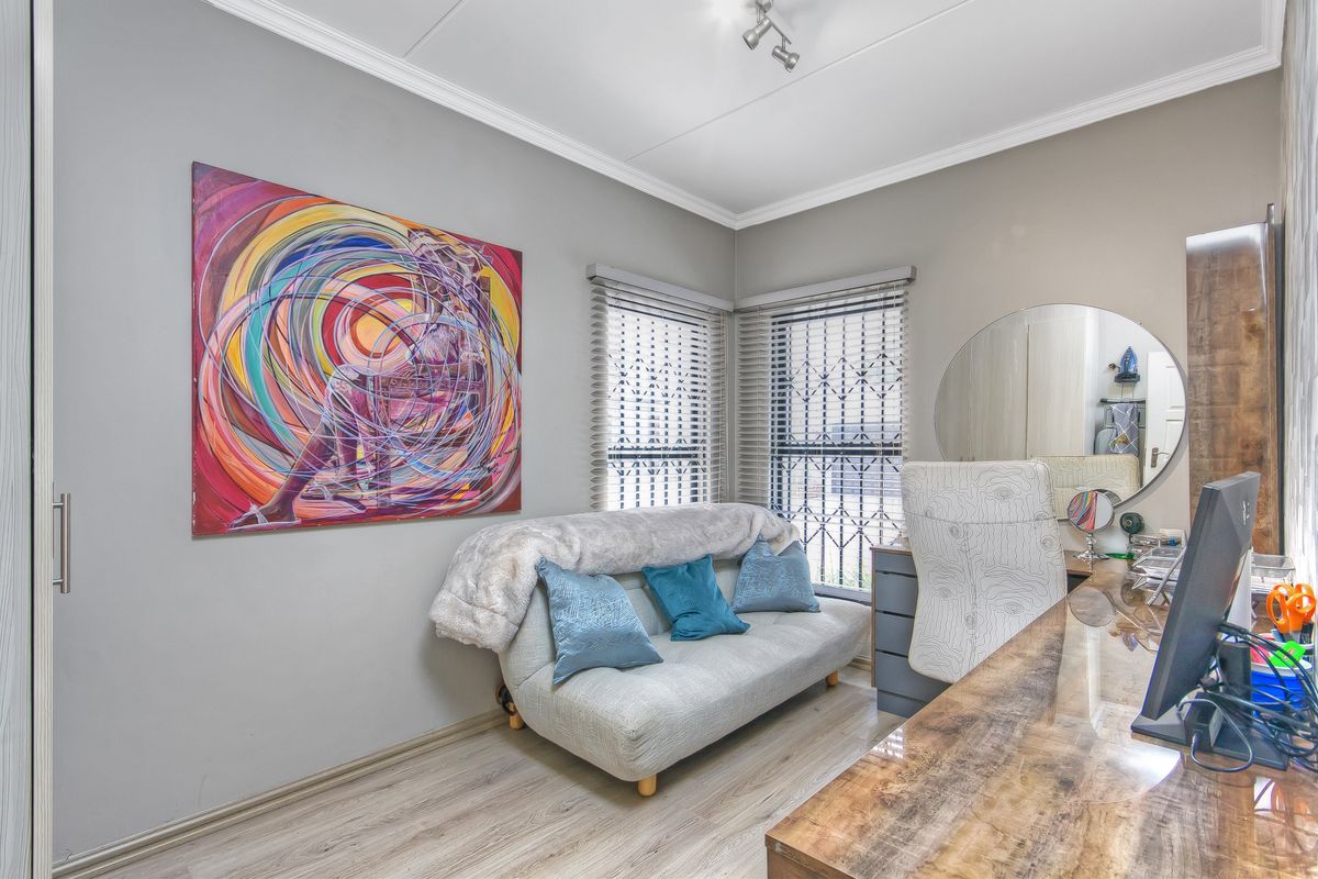 A well-maintained bedroom featuring laminate flooring, built-in desk space, and venetian blinds with security bars on the windows.