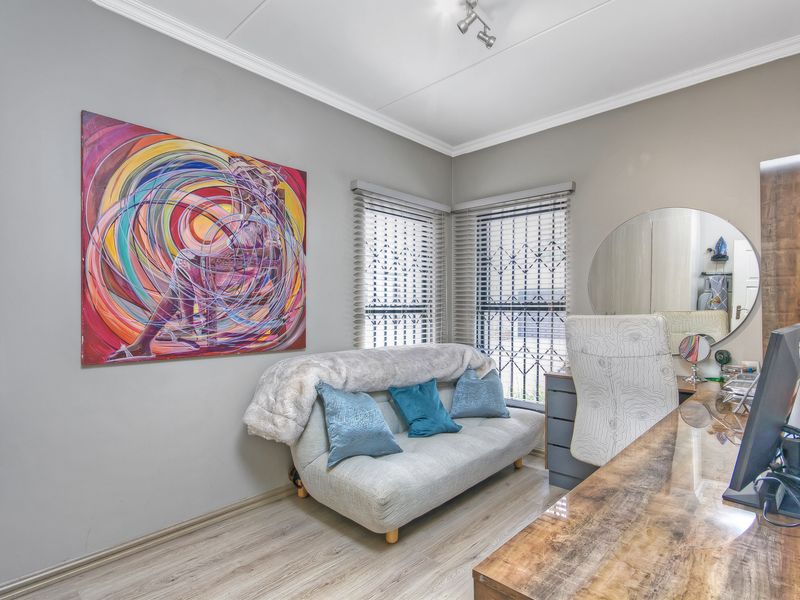 A well-maintained bedroom featuring laminate flooring, built-in desk space, and venetian blinds with security bars on the windows.