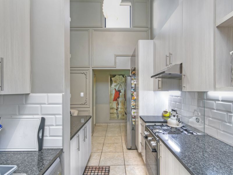 Modern galley-style kitchen featuring granite countertops, subway tile backsplash, gas hob, extractor fan, and ample built-in cabinetry with high ceilings.