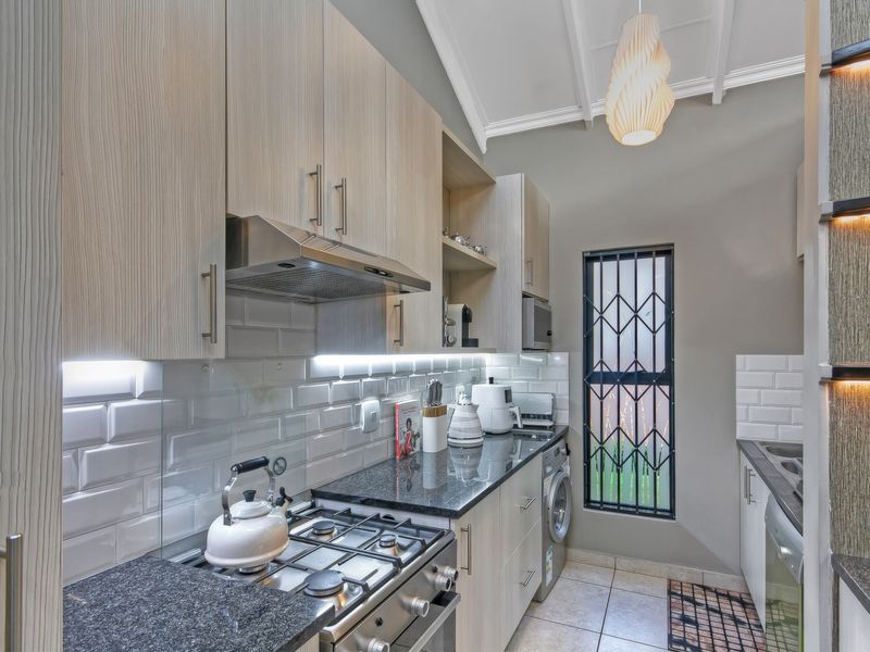 Modern kitchen featuring light wood cabinetry, granite countertops, subway tile backsplash, gas hob, extractor fan, and vaulted ceilings with integrated lighting.