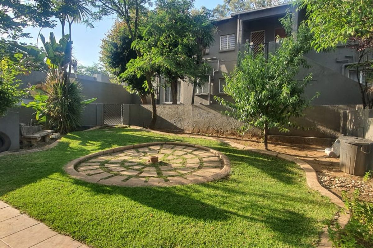 A private rear garden featuring a lawn, a circular paved feature, and a tiled patio area enclosed by boundary walls.
