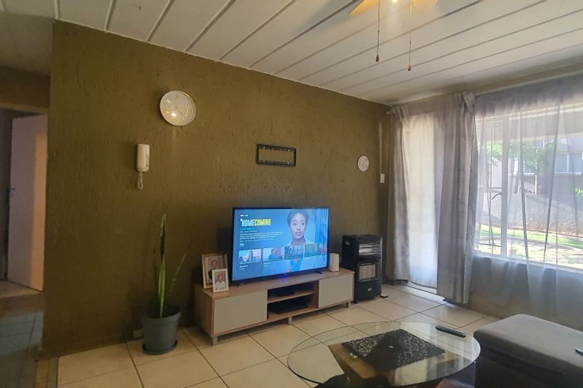 A living room featuring tiled flooring, textured walls, and a large window providing natural light and garden views.