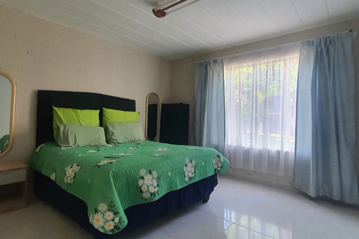 A functional bedroom featuring tiled flooring, built-in wardrobe storage, and large windows allowing natural light.