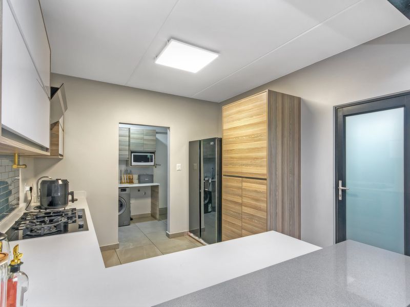 Modern kitchen featuring sleek cabinetry, stone countertops, gas hob, and a subway tile backsplash, with an adjacent scullery area and frosted glass door.