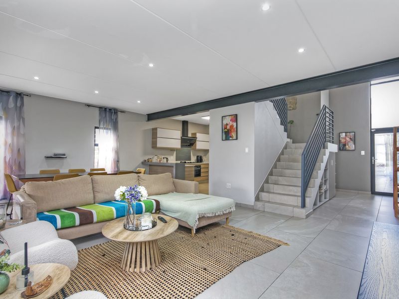 Spacious open-plan living area featuring modern tiled floors, a contemporary staircase, and a functional kitchen with built-in appliances and sleek cabinetry.