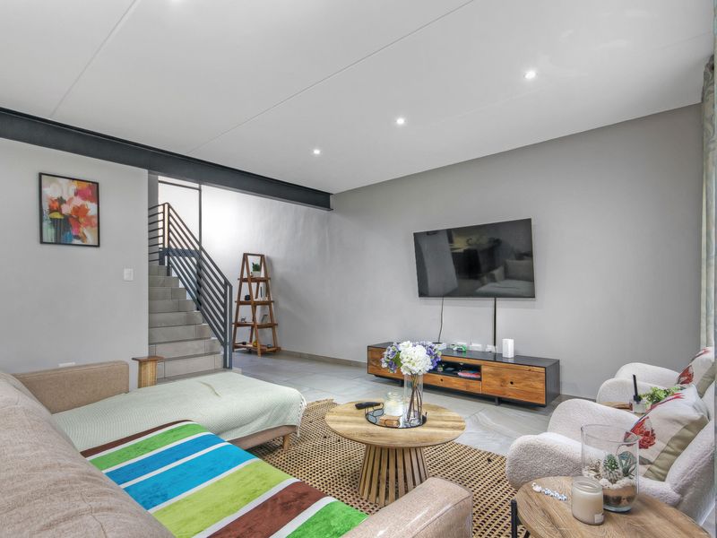 Modern living room featuring tiled floors, recessed lighting, and an open staircase with a metal balustrade, creating a bright and contemporary atmosphere.
