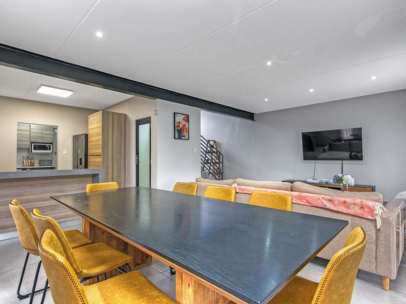 Spacious open-plan living and dining area featuring modern tiled floors, recessed lighting, an exposed structural beam, and a functional kitchen with breakfast bar.
