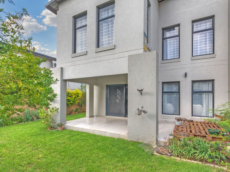 Rear view of the townhouse featuring a covered patio with tiled flooring, sliding glass doors, and a well-maintained garden area.