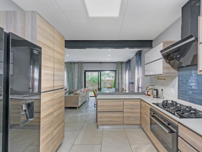 Modern open-plan kitchen and living area featuring contemporary wood-grain cabinetry, gas hob, stone countertops, and seamless flow to the rear patio through sliding doors.