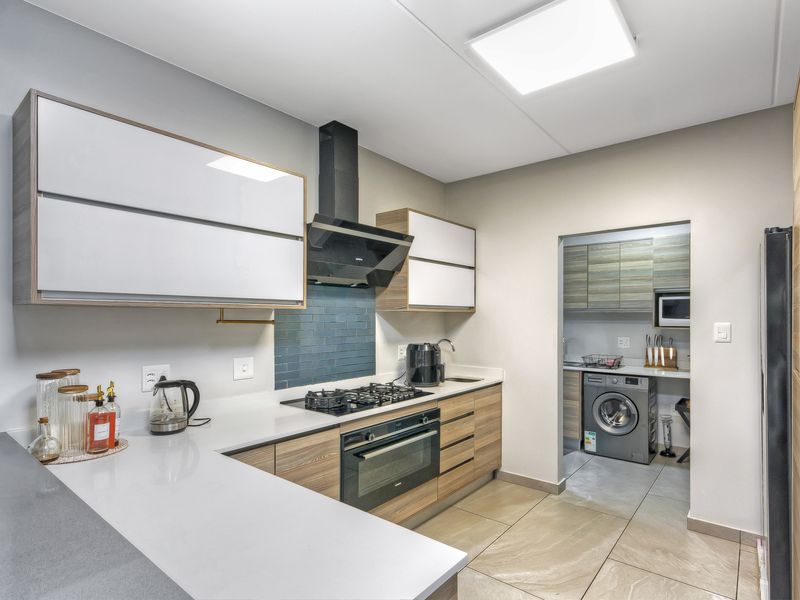 Modern kitchen featuring sleek white and wood-grain cabinetry, quartz countertops, gas hob, extractor fan, and an adjoining scullery area with tiled flooring.
