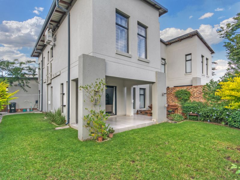 Rear view of the townhouse featuring a covered patio with tiled flooring, overlooking a well-maintained private garden and brick boundary wall.