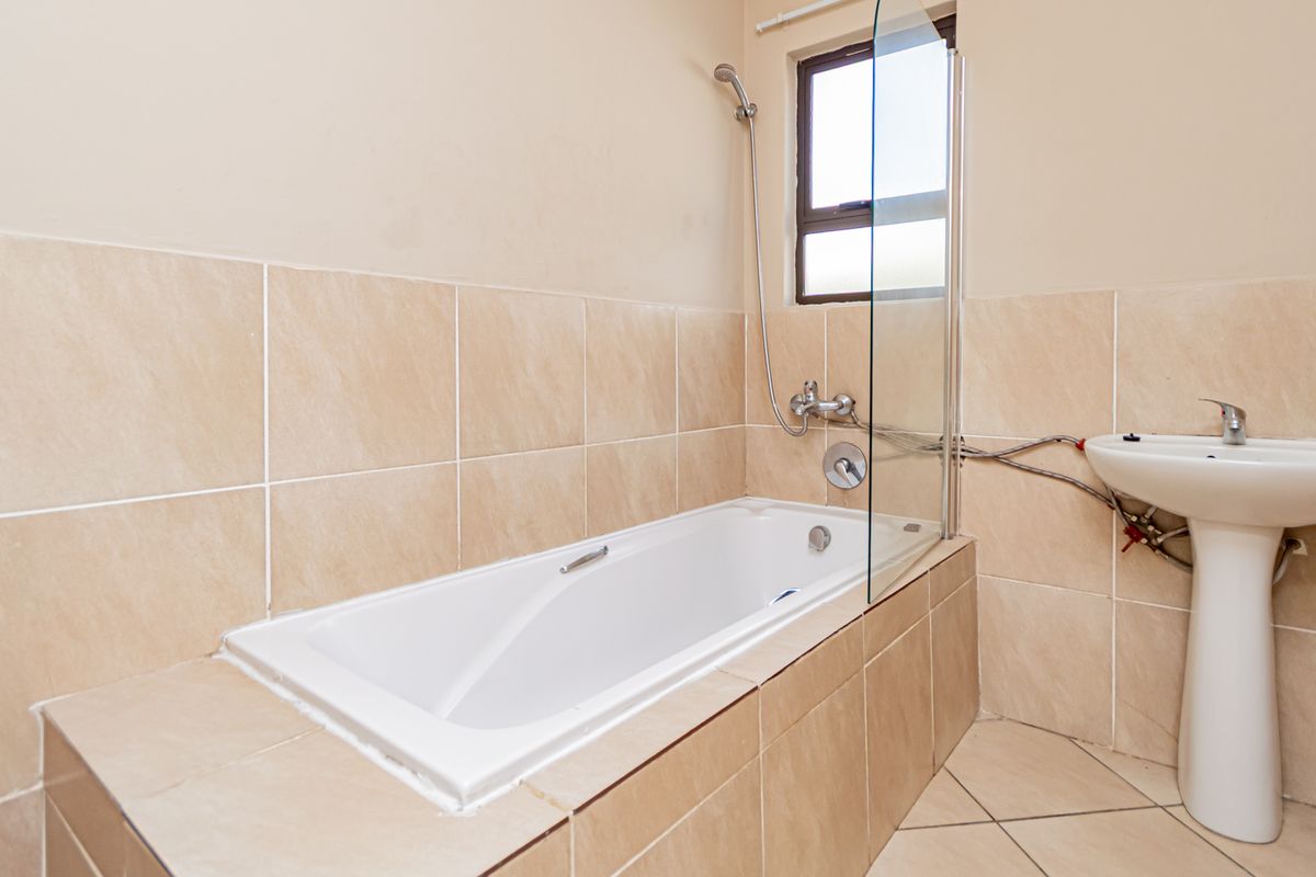 A functional bathroom featuring a built-in bathtub with a glass screen and a pedestal basin, finished with neutral ceramic wall and floor tiling.