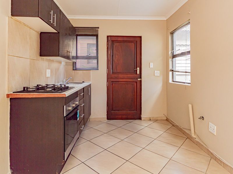A functional kitchen featuring dark cabinetry, a gas hob, built-in oven, tiled flooring, and direct access to an exterior door.
