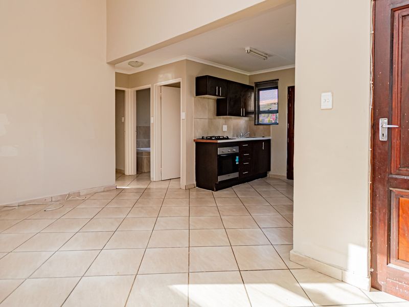 Open plan living area featuring tiled flooring and a compact kitchen with built-in cabinetry, oven, and hob, leading to adjacent rooms.