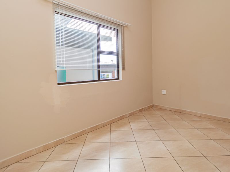 An empty bedroom featuring tiled flooring, neutral wall paint, and a window with fitted blinds.