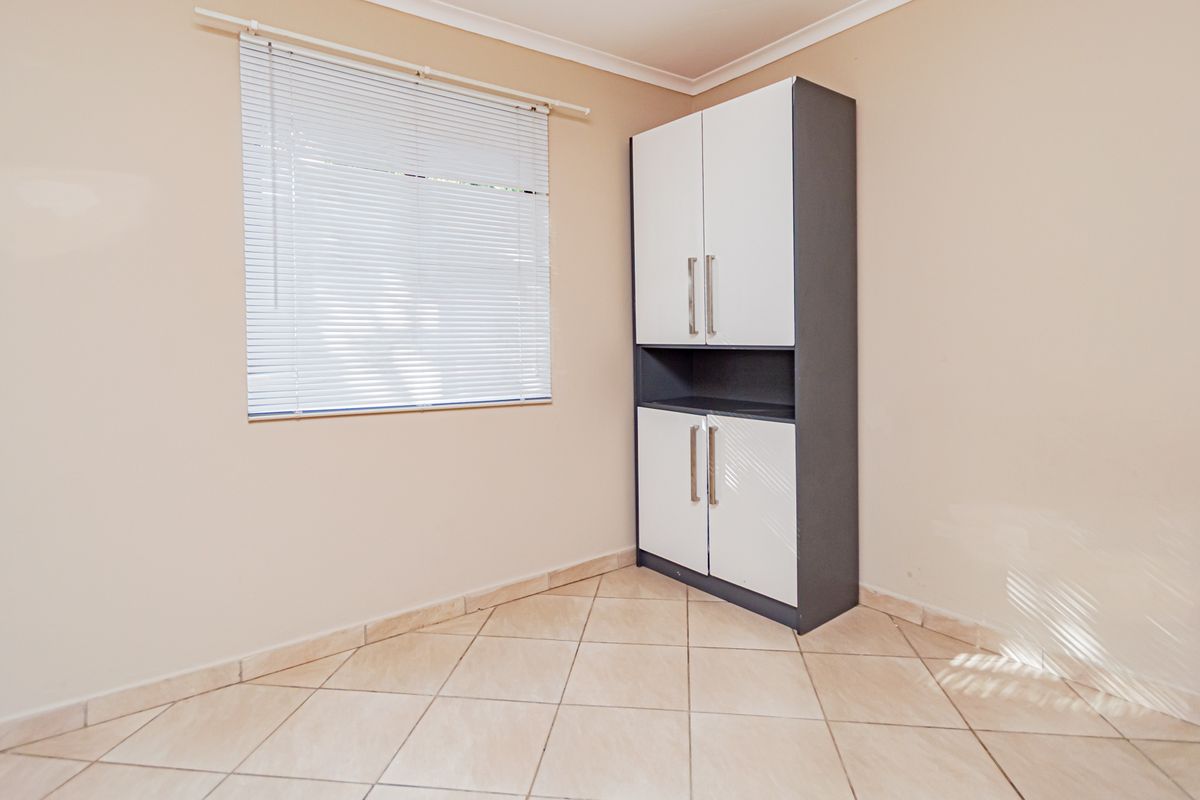 A clean, empty bedroom featuring neutral tiled flooring, a built-in storage cupboard, and venetian blinds.