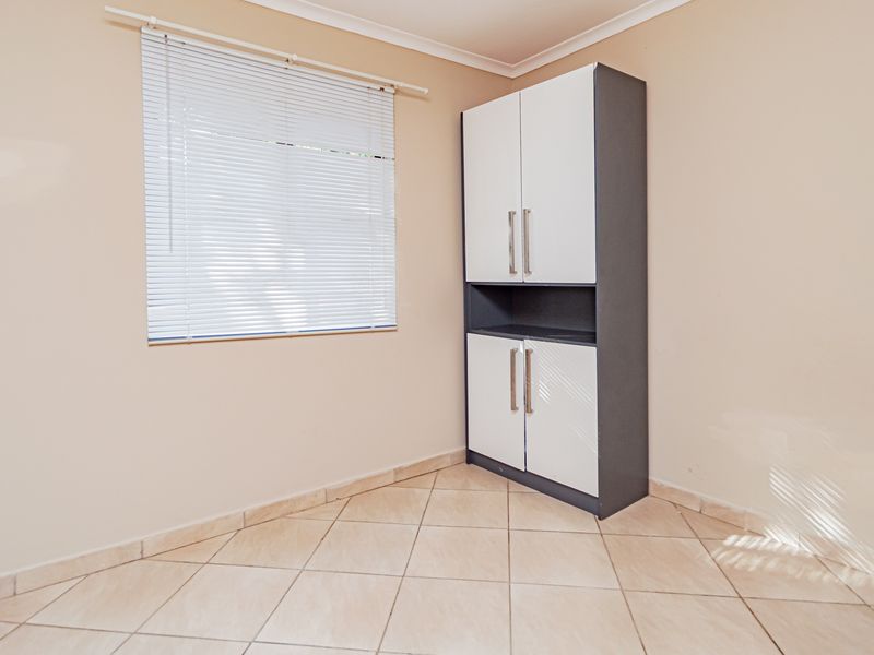 A clean, empty bedroom featuring neutral tiled flooring, a built-in storage cupboard, and venetian blinds.
