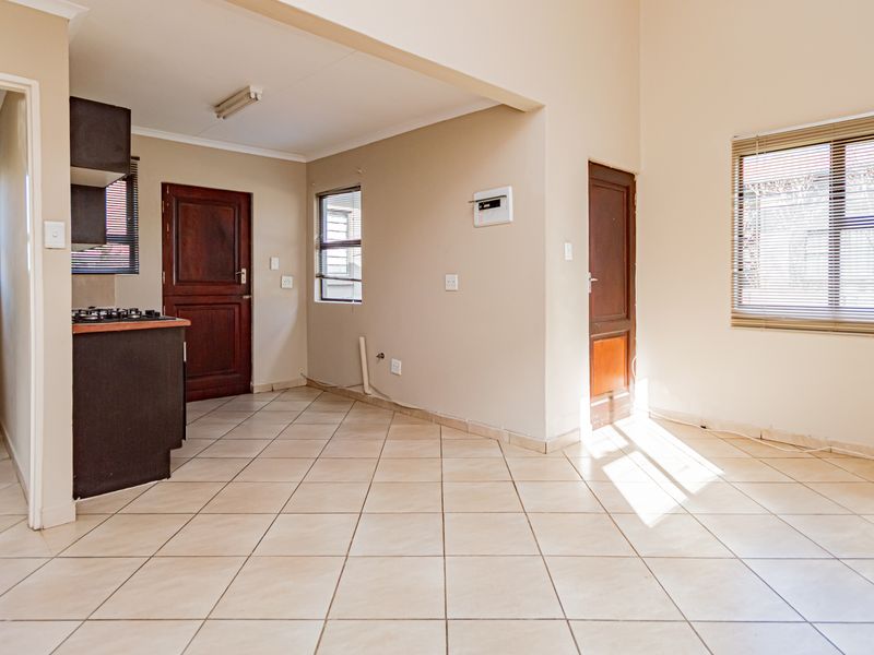 An open-plan living and kitchen area featuring tiled flooring, built-in cabinetry with a gas hob, and an adjacent bathroom.