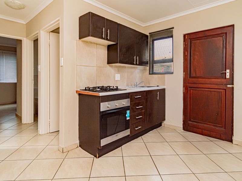 Compact kitchen featuring dark cabinetry, built-in gas hob and oven, stainless steel sink, and tiled flooring.