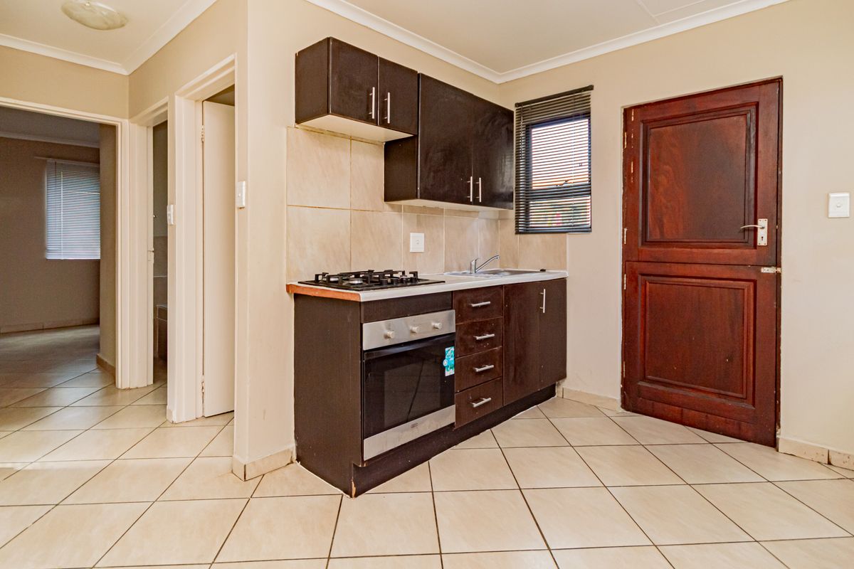 Compact kitchen featuring dark cabinetry, built-in gas hob and oven, stainless steel sink, and tiled flooring.