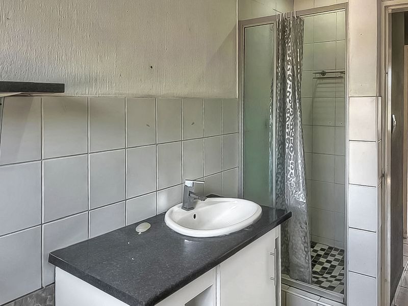 A functional bathroom featuring a vanity with a washbasin, a shower enclosure, and tiled wall finishes, currently showing signs of wear and dated decor.