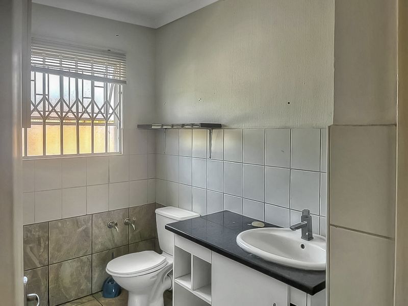 A functional bathroom featuring a vanity with basin, toilet, and tiled walls, equipped with a security gate on the window.