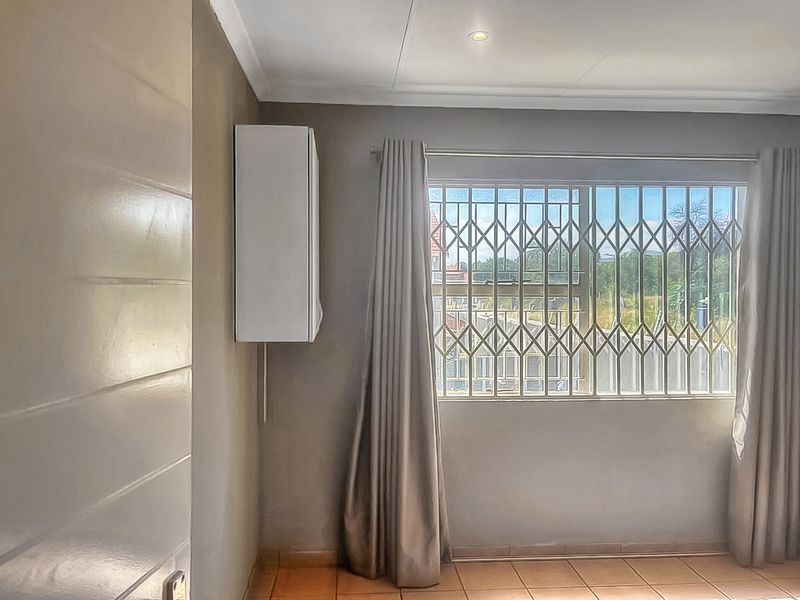 A bright, empty bedroom featuring tiled flooring, recessed ceiling lighting, and a security gate on the window.