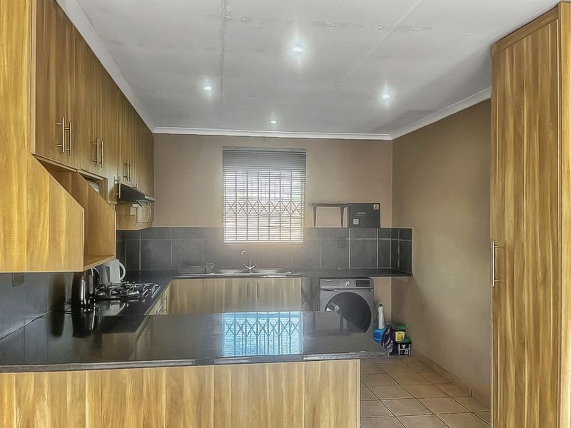 Functional kitchen featuring wood-finish cabinetry, granite countertops, a gas hob, and integrated laundry plumbing, with a window security gate and tiled finishes.
