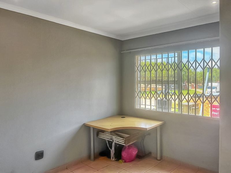 A simple, neutral-toned bedroom featuring tiled flooring, coving, and a window fitted with a security gate.
