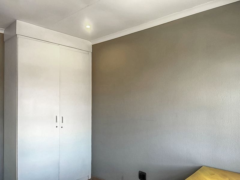 A clean, neutral-toned bedroom featuring a built-in white wardrobe and simple cove cornicing, offering a blank canvas for personalization.