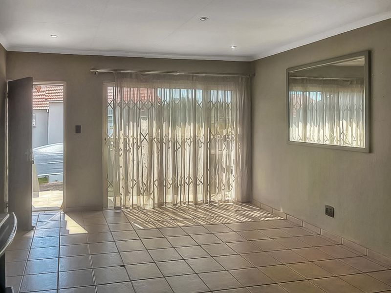 A spacious, empty living room featuring tiled flooring, recessed downlights, and a sliding glass door with a security gate leading to the exterior.