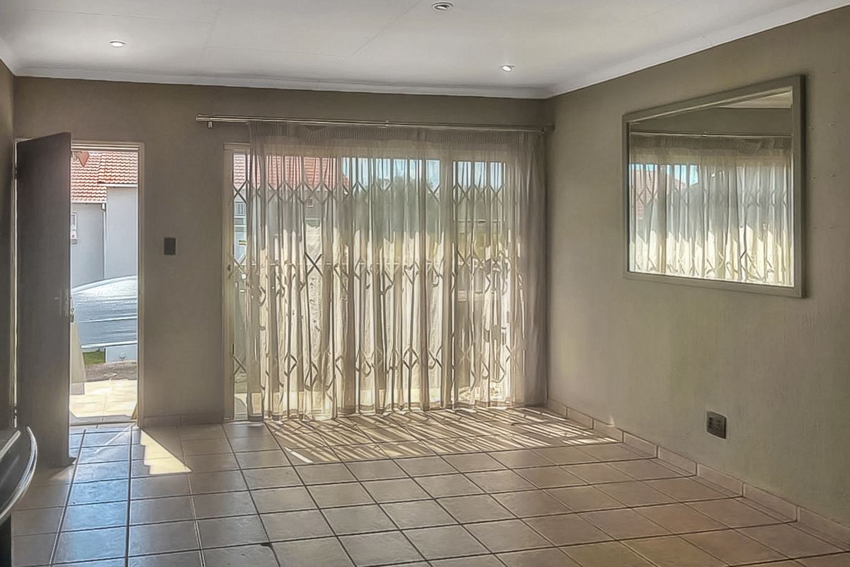 A spacious, empty living room featuring tiled flooring, recessed downlights, and a sliding glass door with a security gate leading to the exterior.