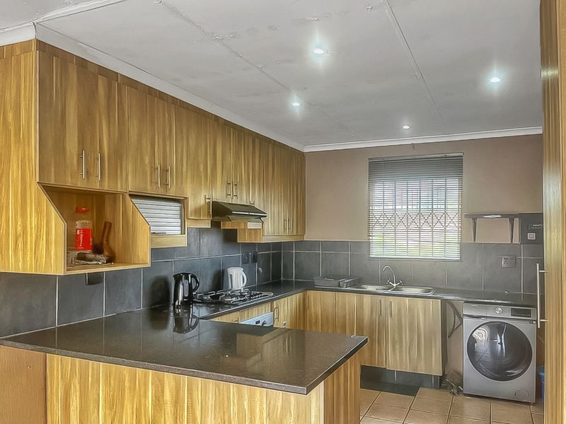 Functional kitchen featuring wood-look cabinetry, dark granite countertops, gas hob, extractor fan, and tiled backsplash with integrated laundry appliance space.