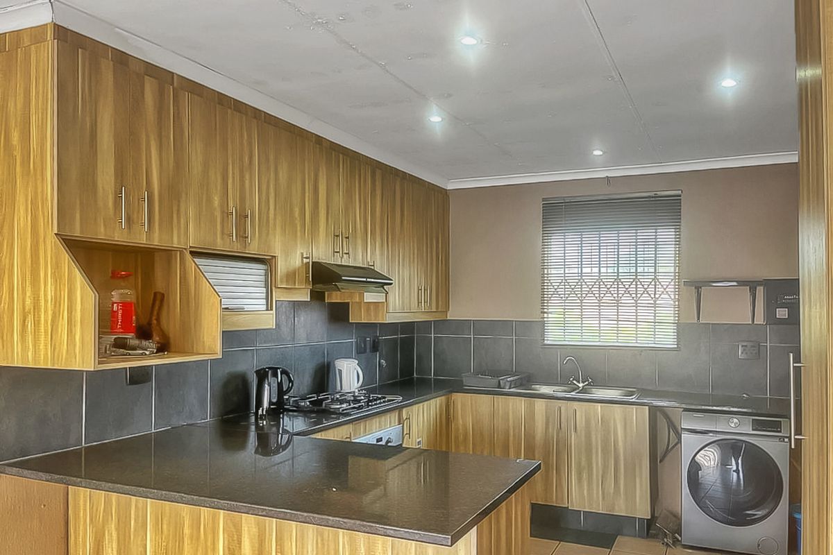 Functional kitchen featuring wood-look cabinetry, dark granite countertops, gas hob, extractor fan, and tiled backsplash with integrated laundry appliance space.