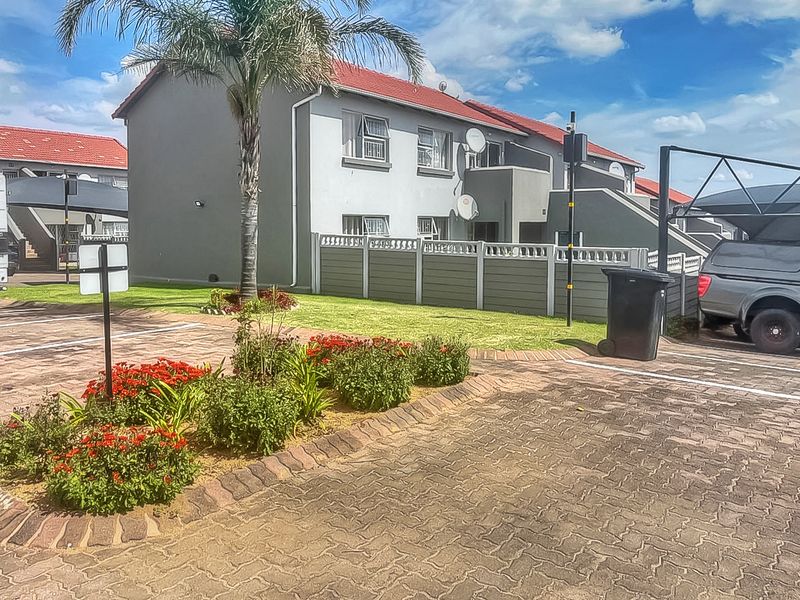 Exterior view of the apartment complex featuring a paved driveway, landscaped garden beds, and dedicated carport parking areas.