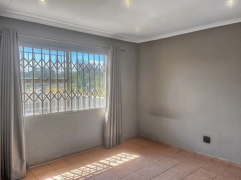 A bright, empty bedroom featuring tiled flooring, recessed downlights, and a window fitted with a security gate.