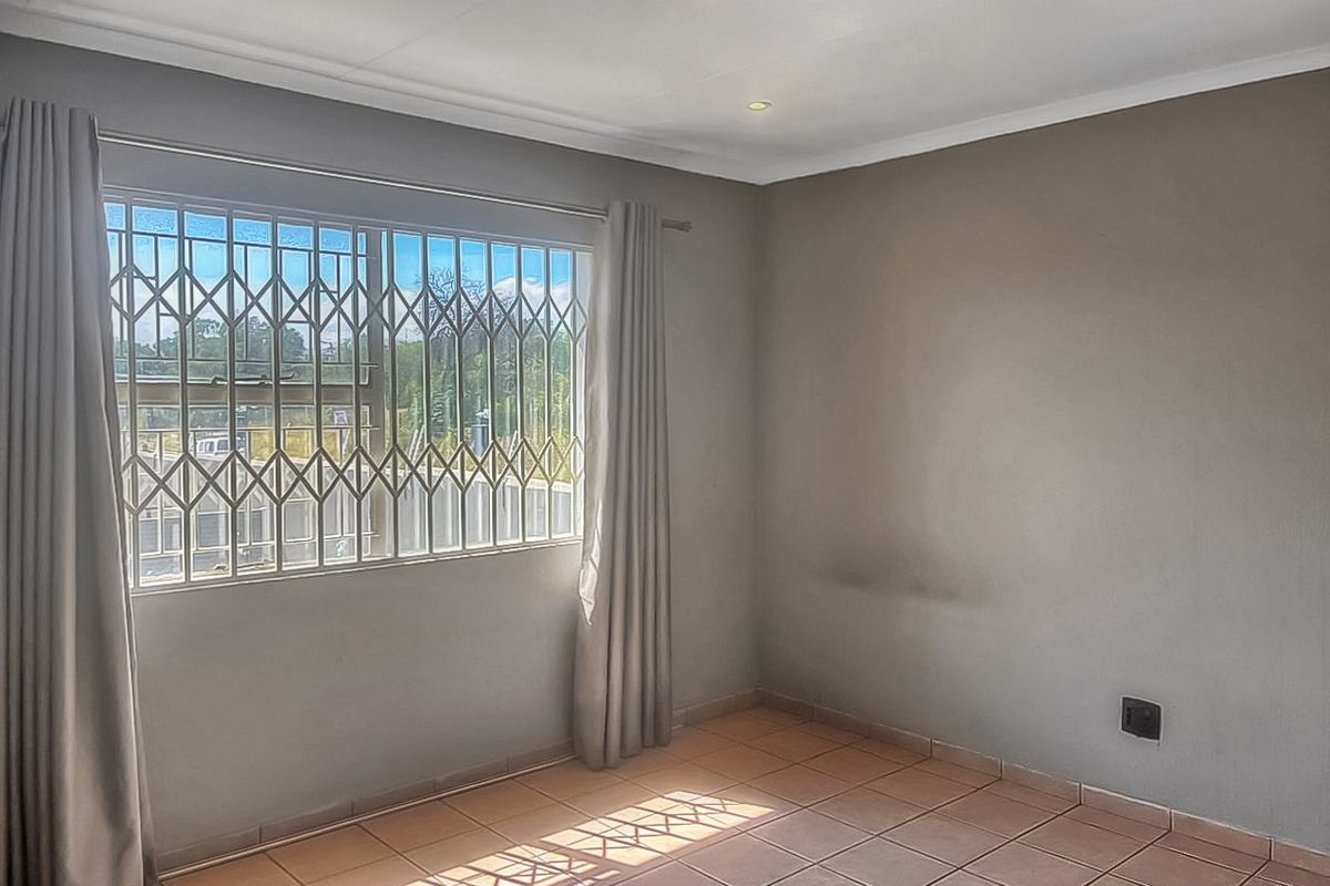 A bright, empty bedroom featuring tiled flooring, recessed downlights, and a window fitted with a security gate.
