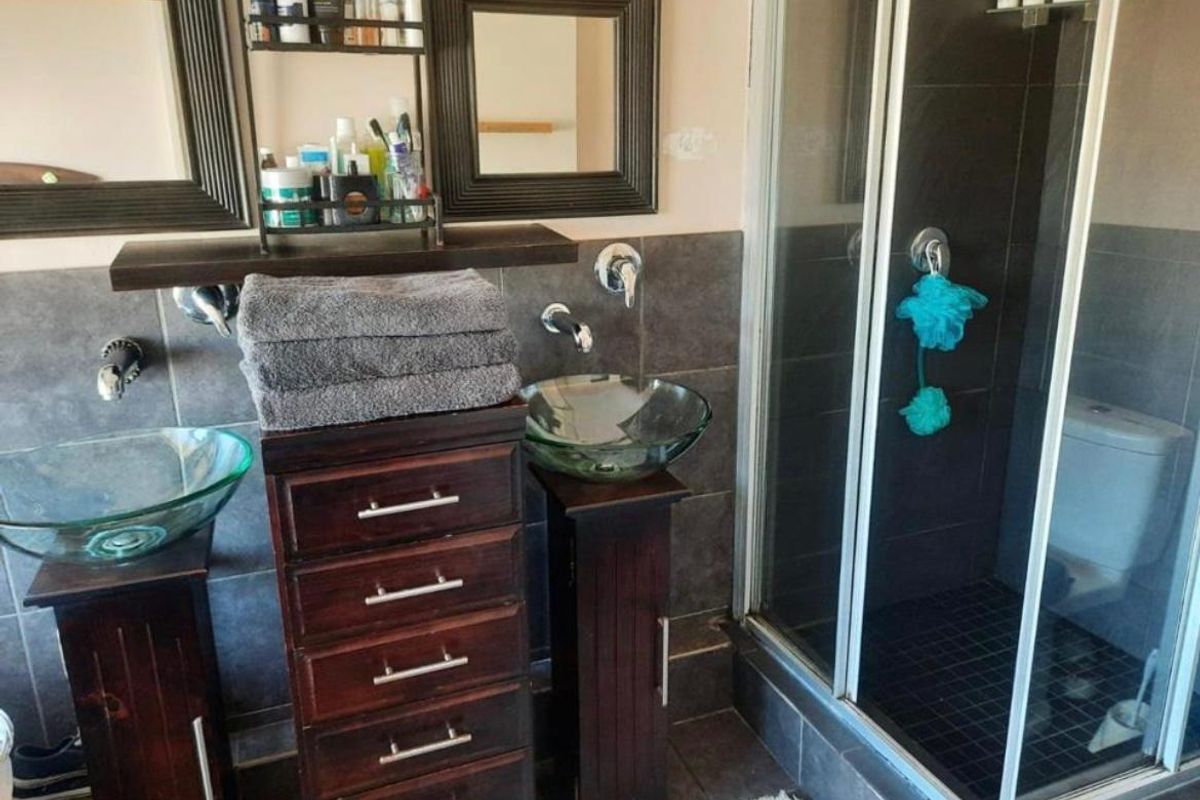 Bathroom featuring dual glass vessel sinks with wall-mounted faucets, dark tiled finishes, and a separate shower enclosure.