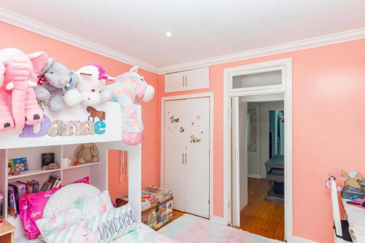 A bright bedroom featuring timber flooring, built-in cupboards with overhead storage, and classic cornicing details.