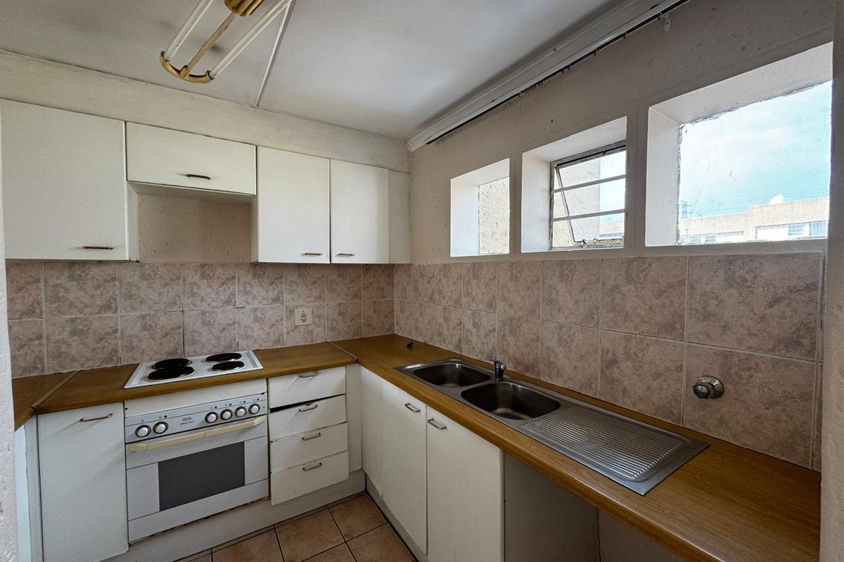 A functional kitchen featuring built-in cabinetry, laminate countertops, a double sink, and an integrated electric oven and hob, ready for a modern update.