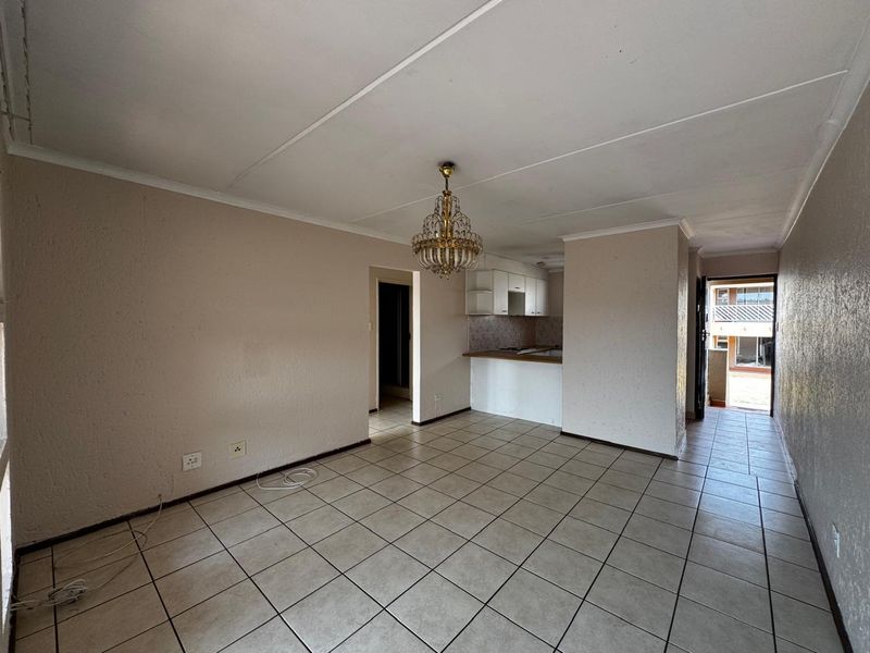 An open-plan living and kitchen area featuring tiled flooring, neutral walls, and a functional kitchen layout, offering a blank canvas for modern updates.