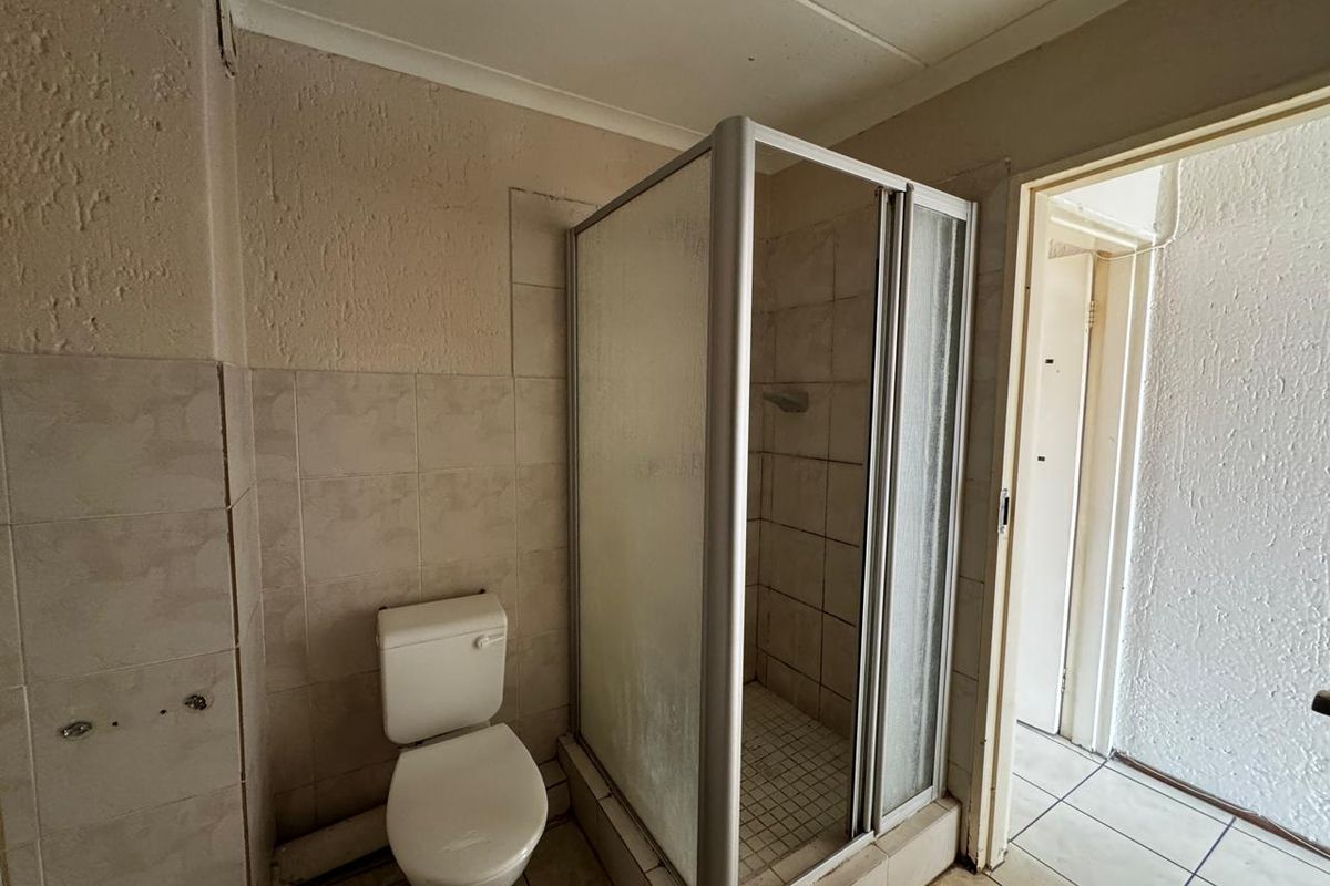 A functional bathroom featuring a shower enclosure and toilet, with tiled walls and flooring, requiring cosmetic updates to modernize the space.