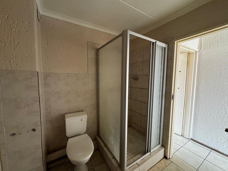A functional bathroom featuring a shower enclosure and toilet, with tiled walls and flooring, requiring cosmetic updates to modernize the space.