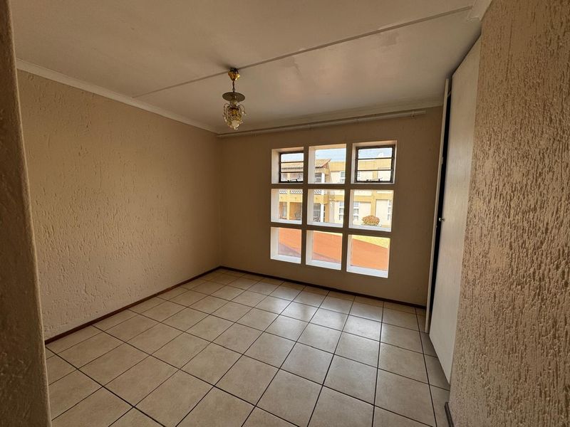 An empty bedroom featuring tiled flooring, a built-in cupboard, and a large multi-pane window providing natural light.